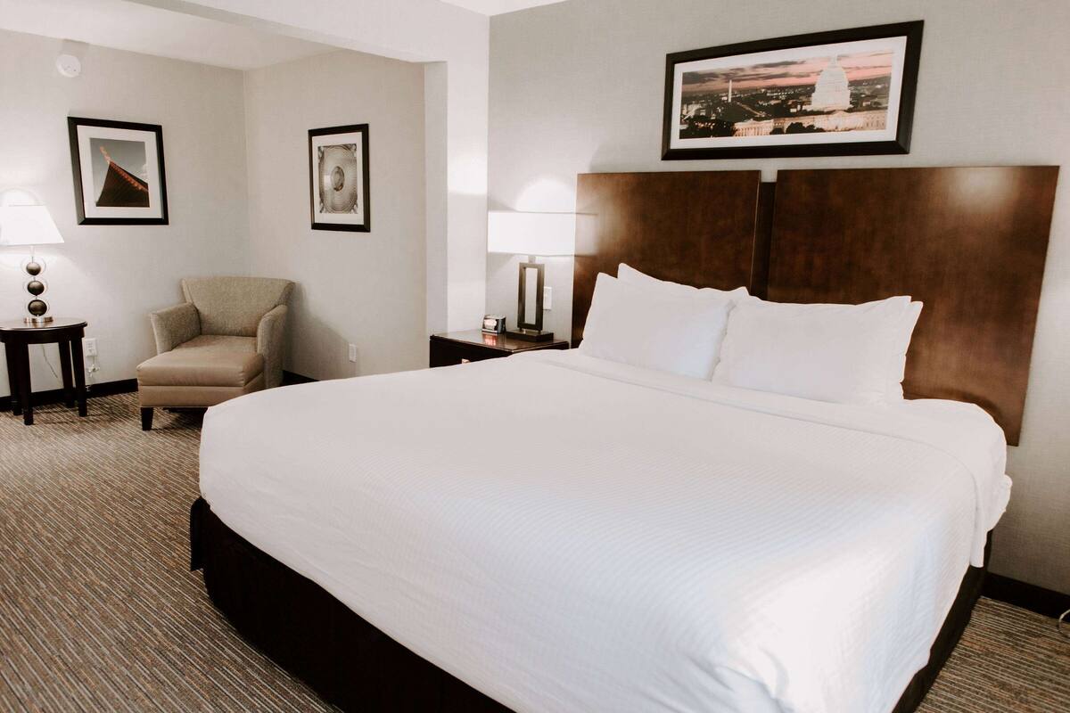 Een hotelkamer met een groot bed, een stoel, een nachtkastje en een lamp.