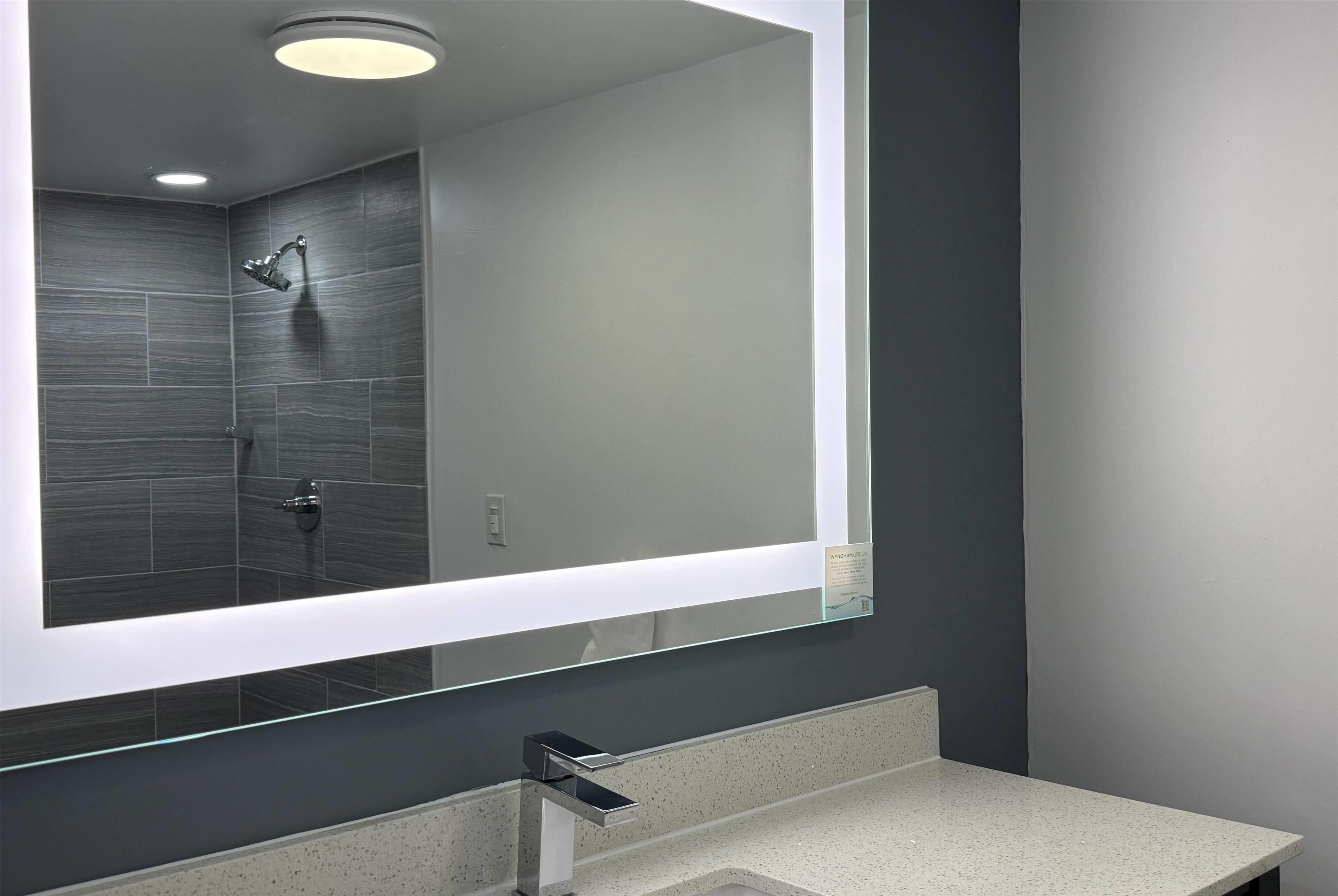 Un baño moderno con un espejo grande, ducha y encimera.