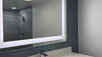 Un baño moderno con un espejo grande, ducha y encimera.