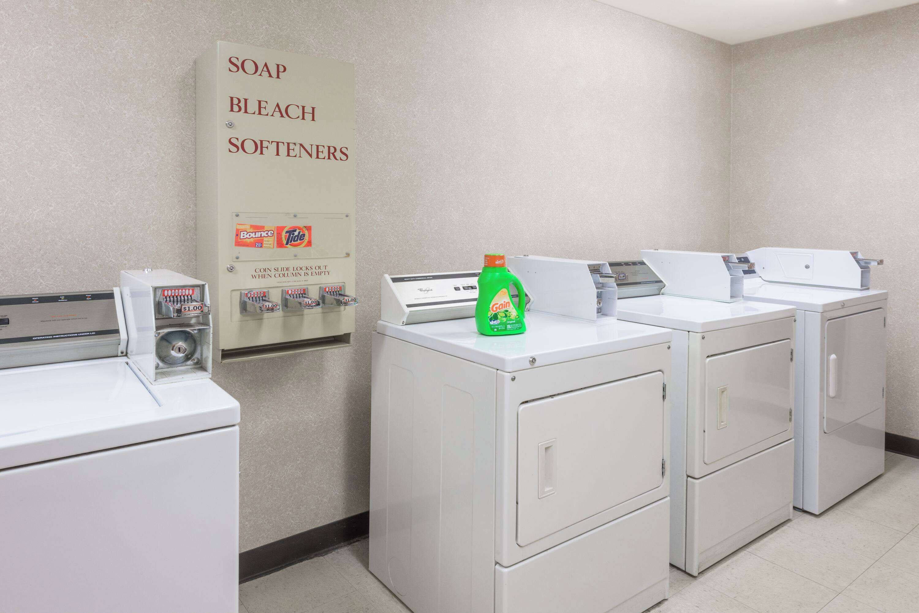 A laundry facility with washers and dryers, a soap and bleach sign, and a bottle of liquid soap.