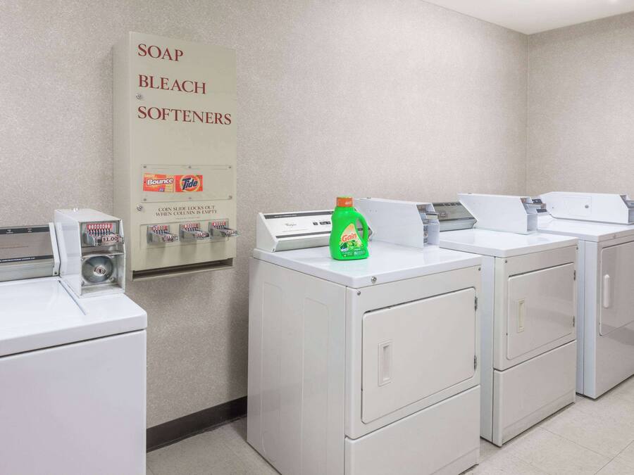 A laundry facility with washers and dryers, a soap and bleach sign, and a bottle of liquid soap.