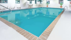 Uma piscina interior com borda azulejada, cadeiras de descanso e plantas em vasos.