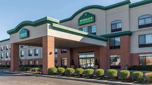 Um hotel Wingate by Wyndham com fachada de tijolos, toldo verde e entrada coberta.