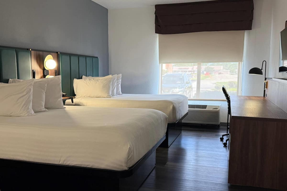 Habitación de hotel con dos camas, un escritorio y una ventana con vista a la calle.