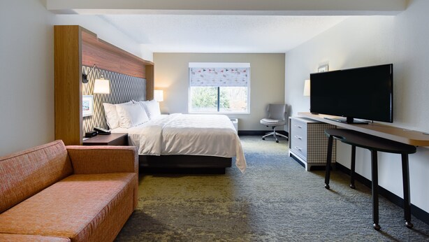 A hotel room with a bed, a desk with a television, a chair, a sofa, and a window with blinds. - Holiday Inn Allentown-Bethlehem by IHG (Allentown)