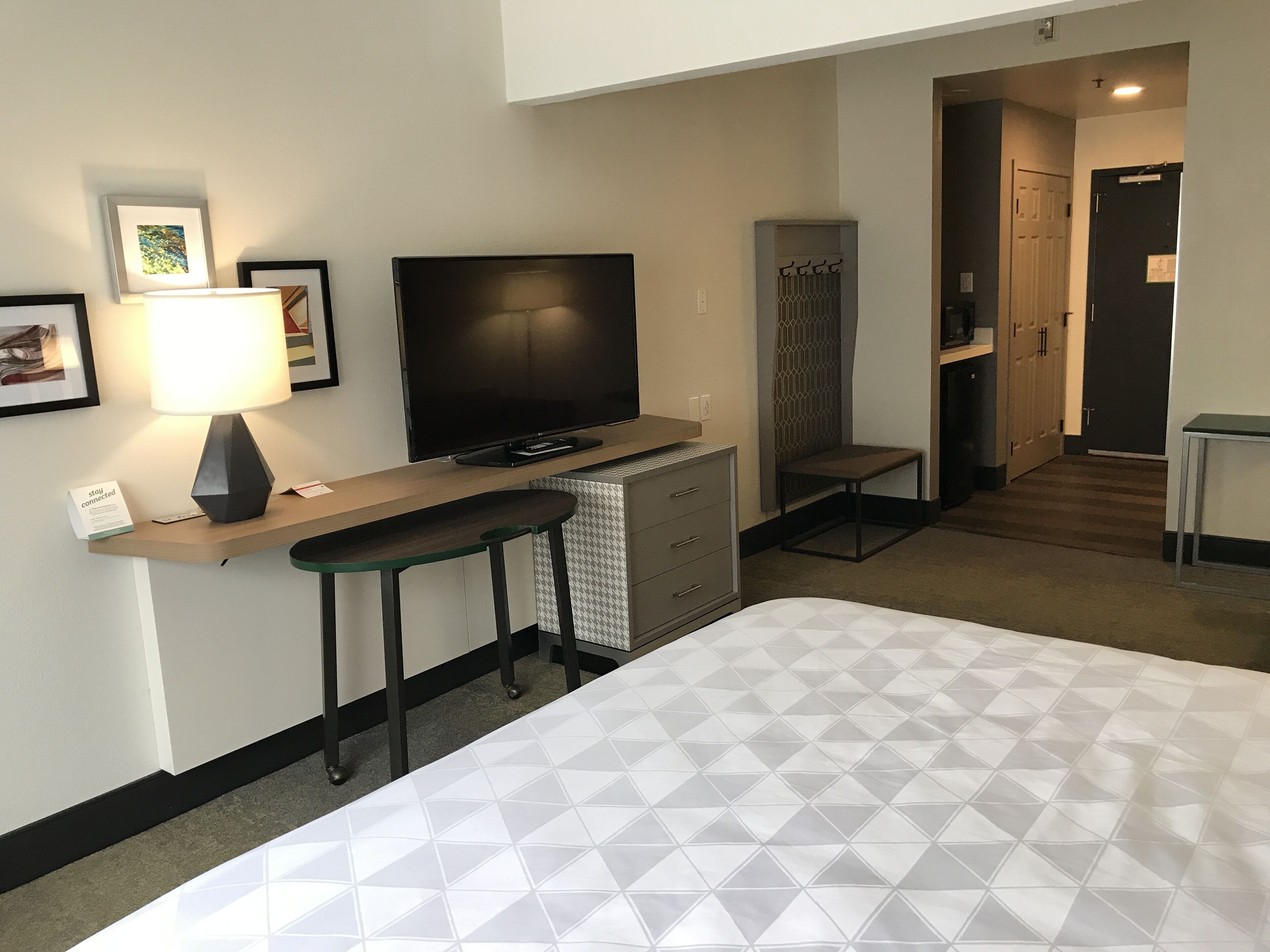 Una habitación de hotel con una cama, un escritorio con lámpara, un televisor y un armario.