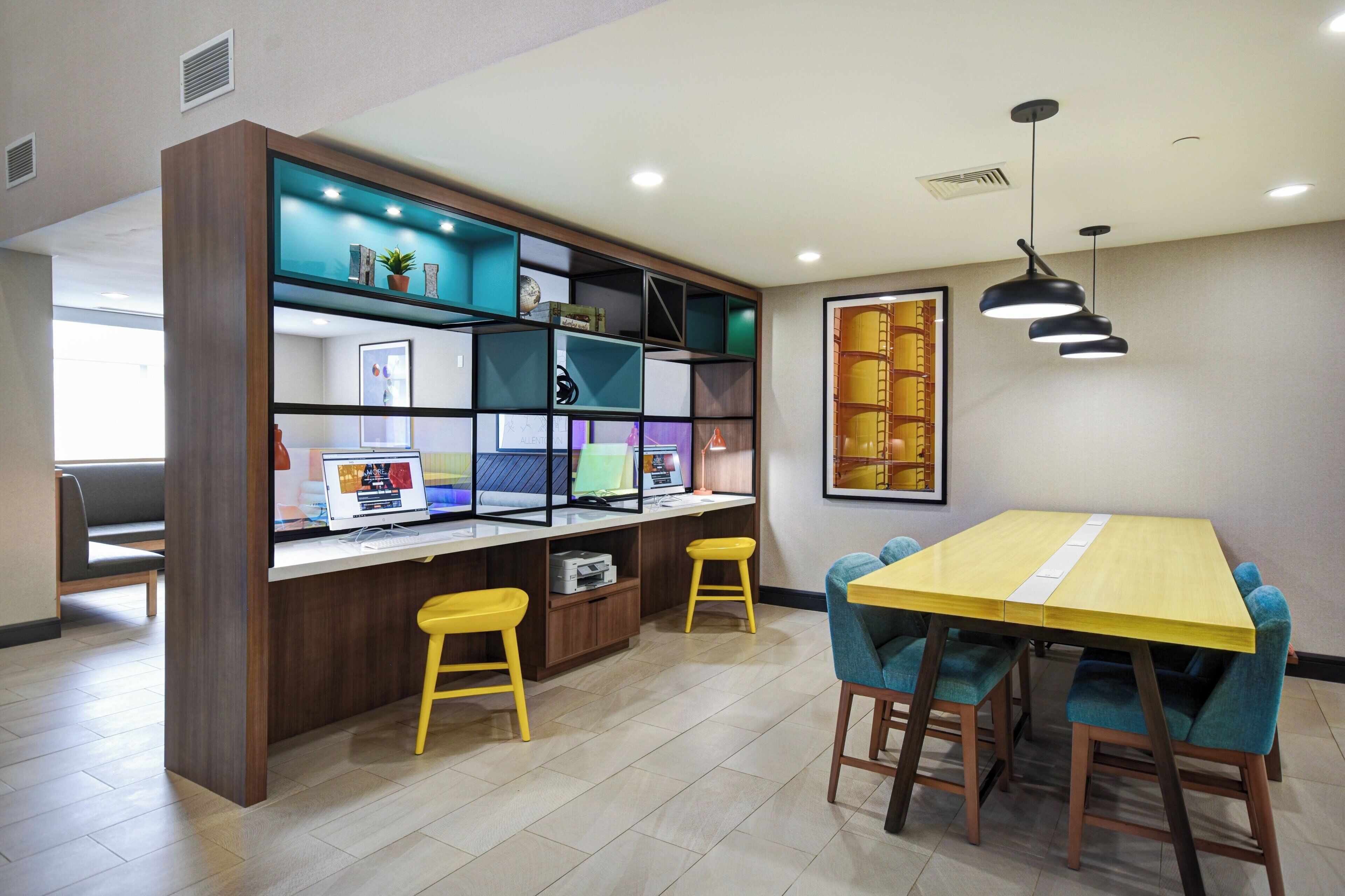 Un interior moderno con un escritorio de madera, dos taburetes amarillos, una mesa amarilla y una estantería con diversos objetos.