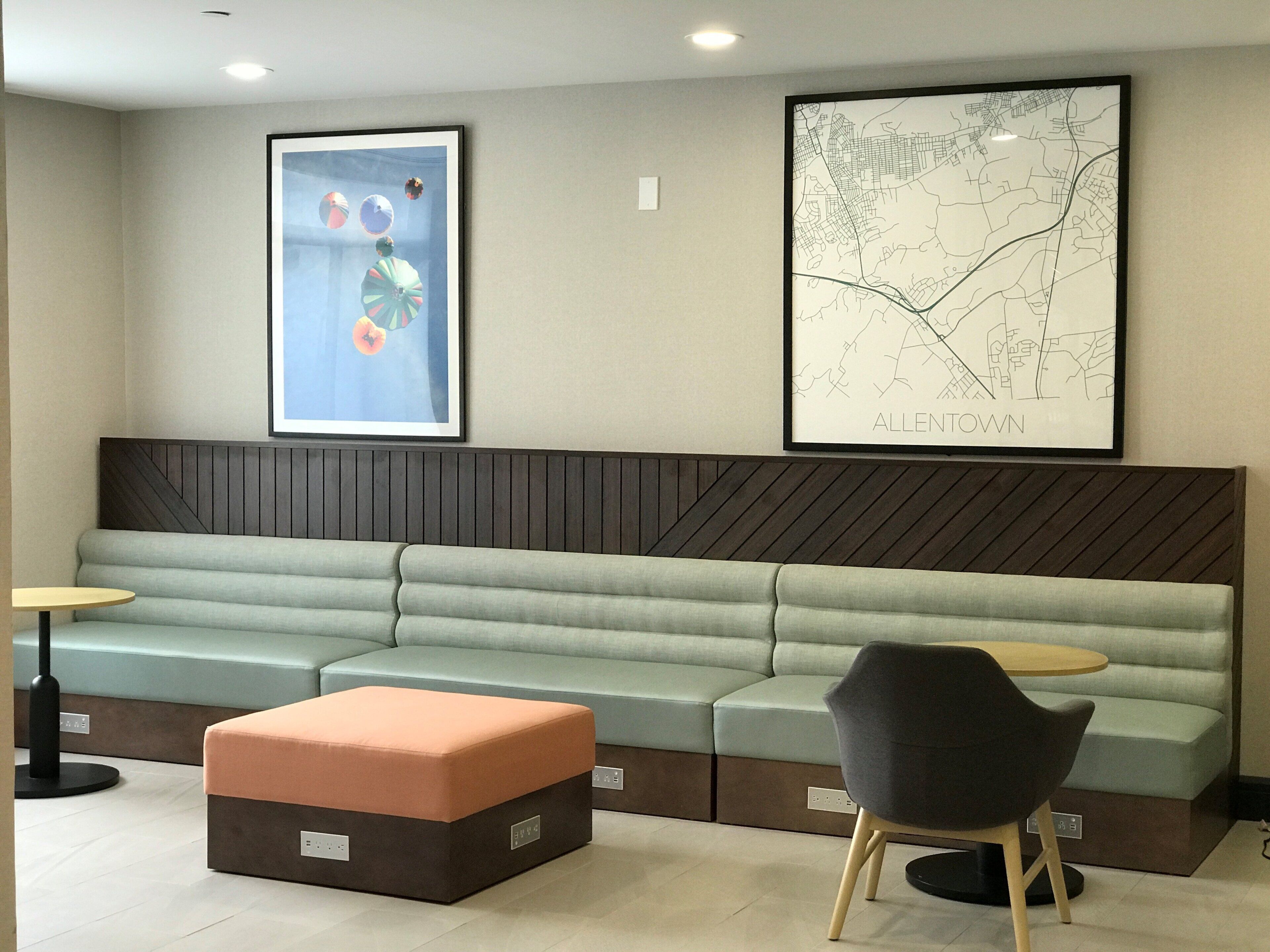 A modern waiting area with a sofa, ottoman, and chairs, a wall-mounted map, and abstract art.