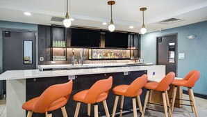 Un espace bar doté d’un comptoir blanc, de plusieurs tabourets et d’une variété de bouteilles et de verres.