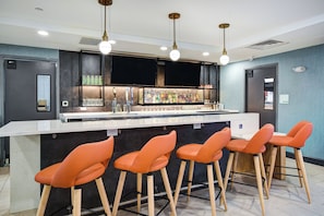 A bar area with a white countertop, multiple stools, and a variety of bottles and glasses. - Holiday Inn Allentown-Bethlehem by IHG (Allentown)