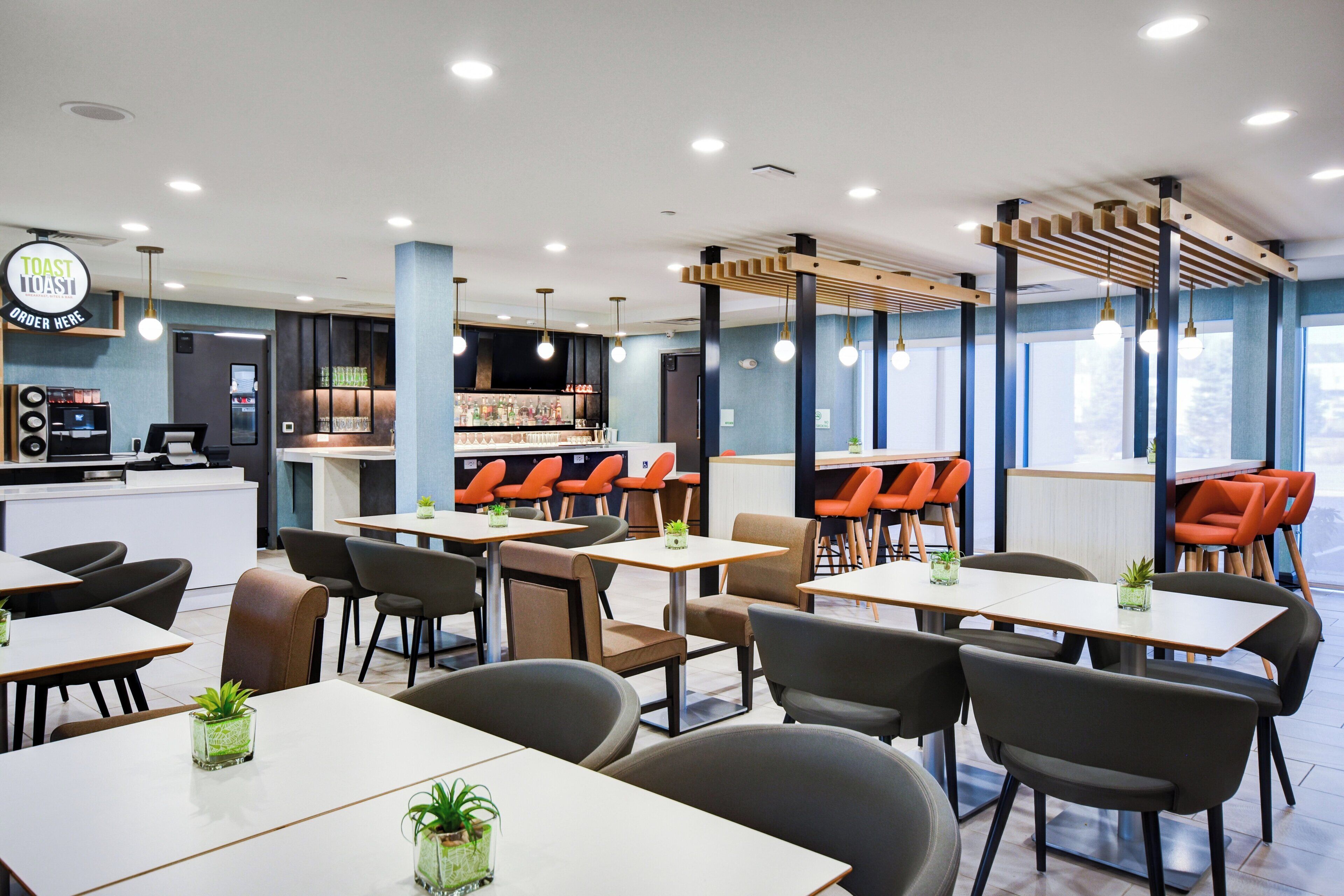 A modern restaurant with multiple seating areas, including tables and booths, and a bar counter.