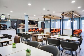 Un restaurante moderno con varias zonas de estar, incluyendo mesas y cabinas, y una barra.