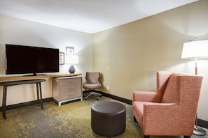 Ein Hotelzimmer mit Flachbildfernseher, Schreibtisch, Stuhl, Lampe und einem kleinen Hocker.