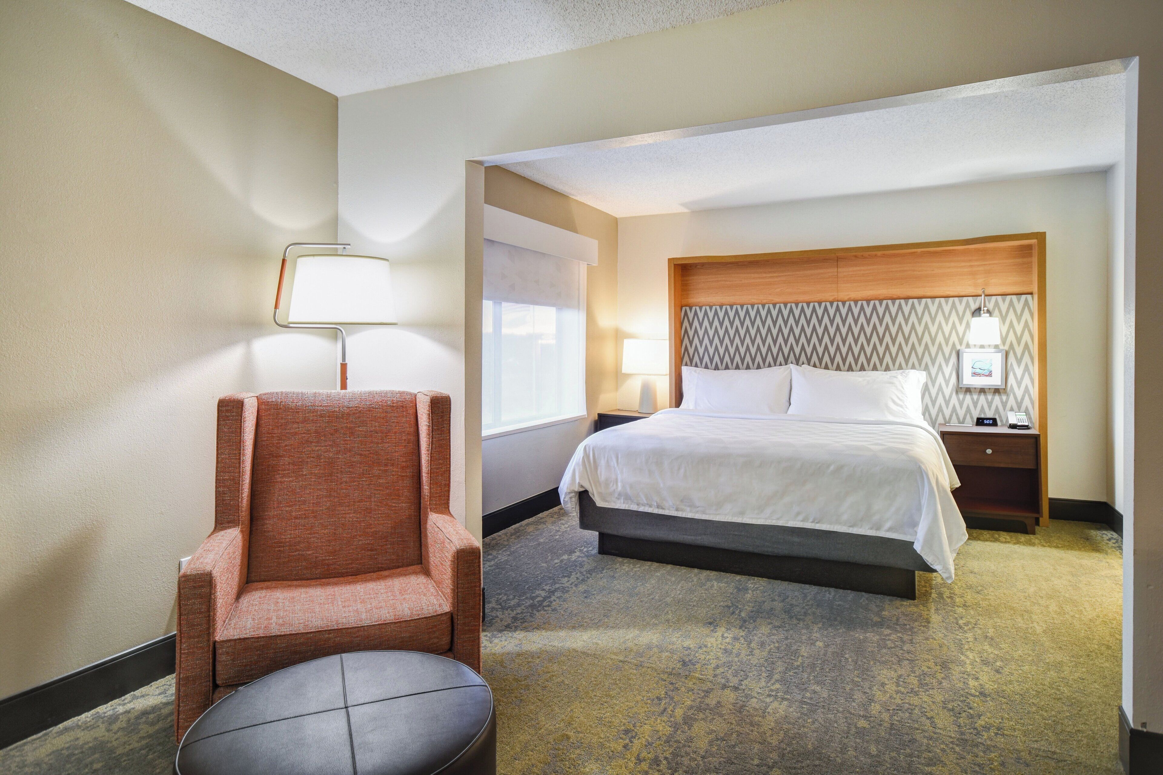 A hotel room with a bed, a chair, a nightstand, a lamp, and a wall with a patterned design.