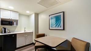 Une chambre d’hôtel compacte dotée d’une kitchenette, d’une table à manger avec deux chaises et d’une œuvre d’art encadrée au mur.