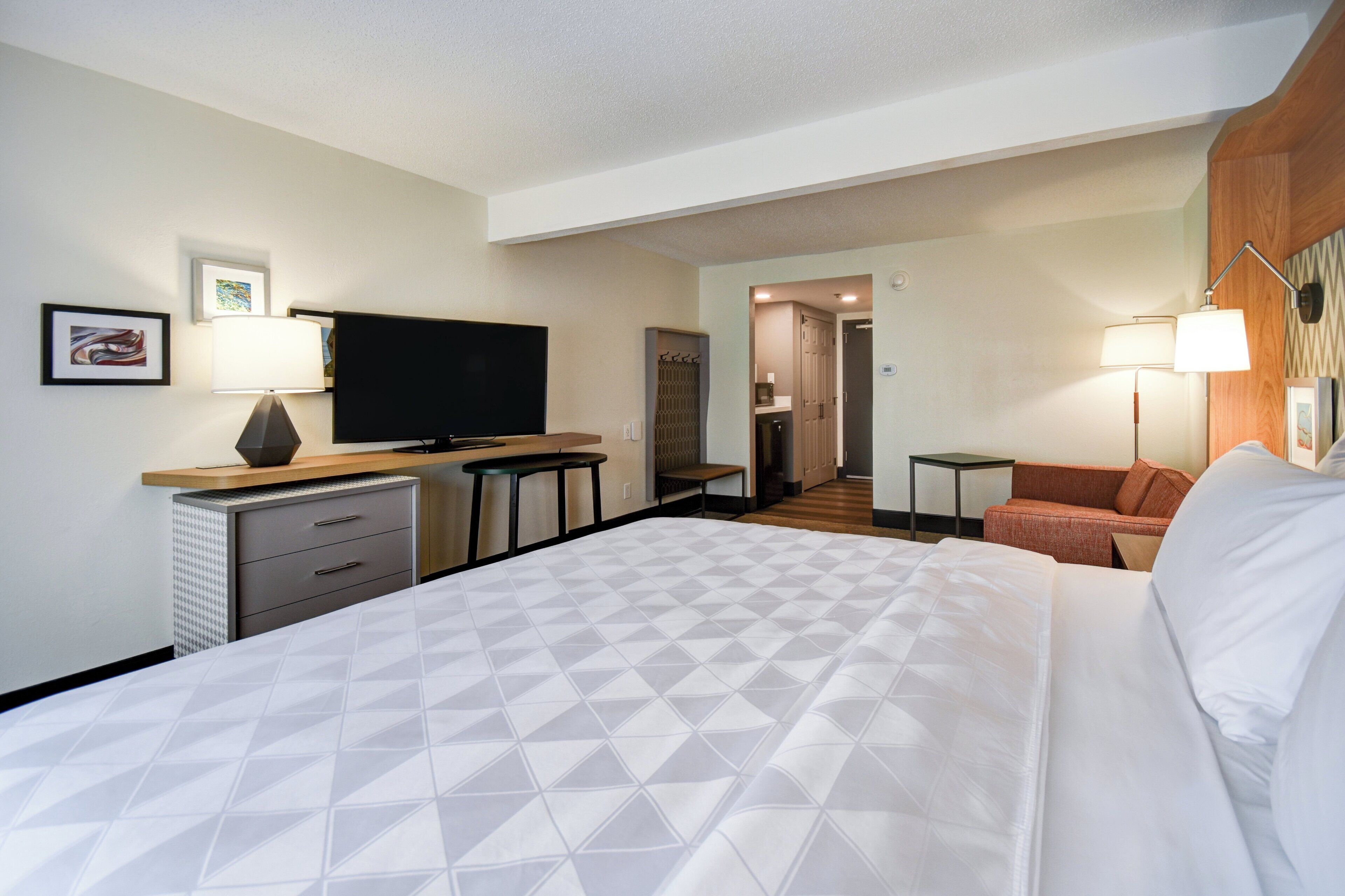 A hotel room with a bed, a desk, a television, a chair, and a small table.