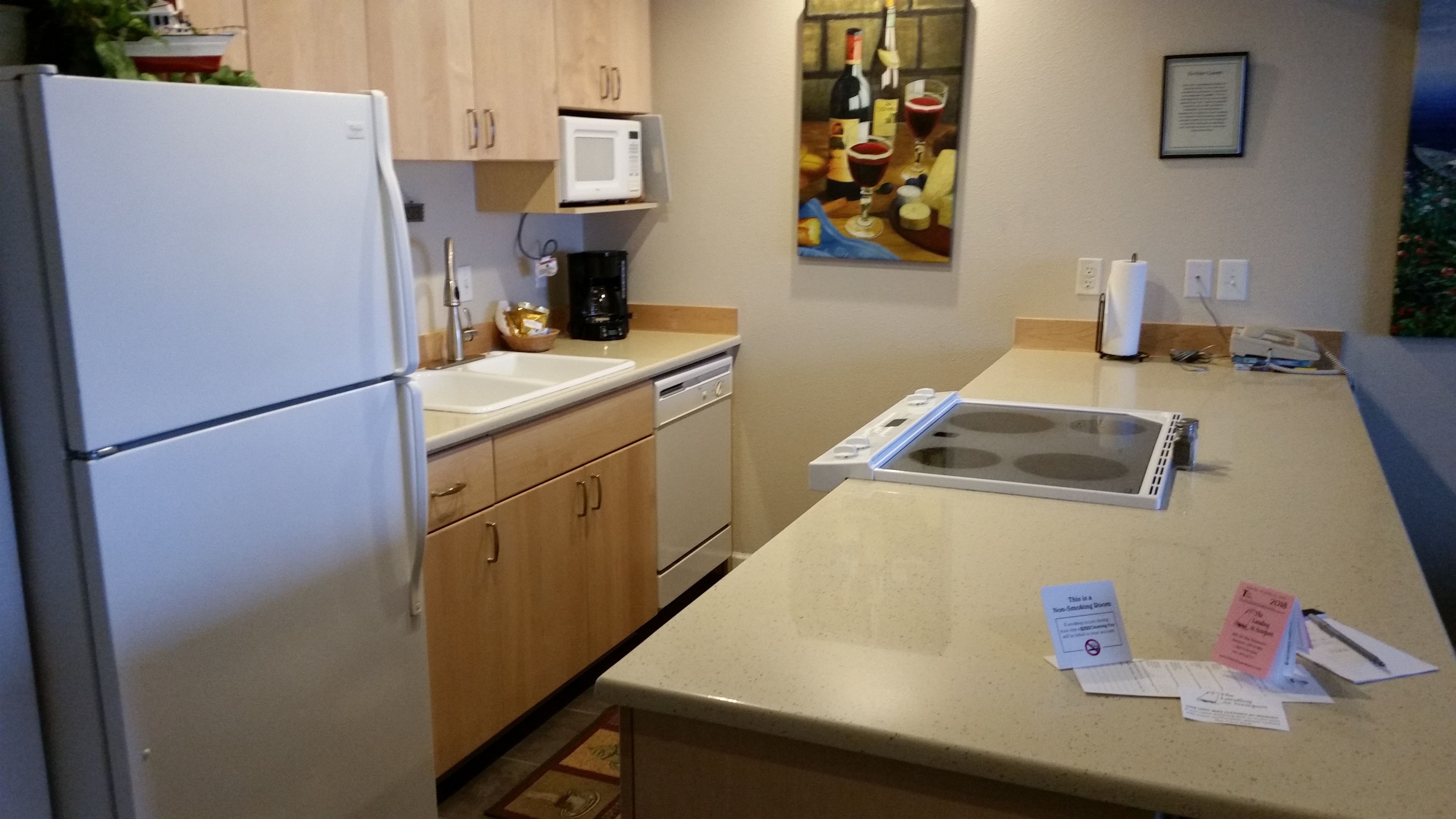 A kitchen with a refrigerator, microwave, sink, and stove. There are wooden cabinets and a countertop.