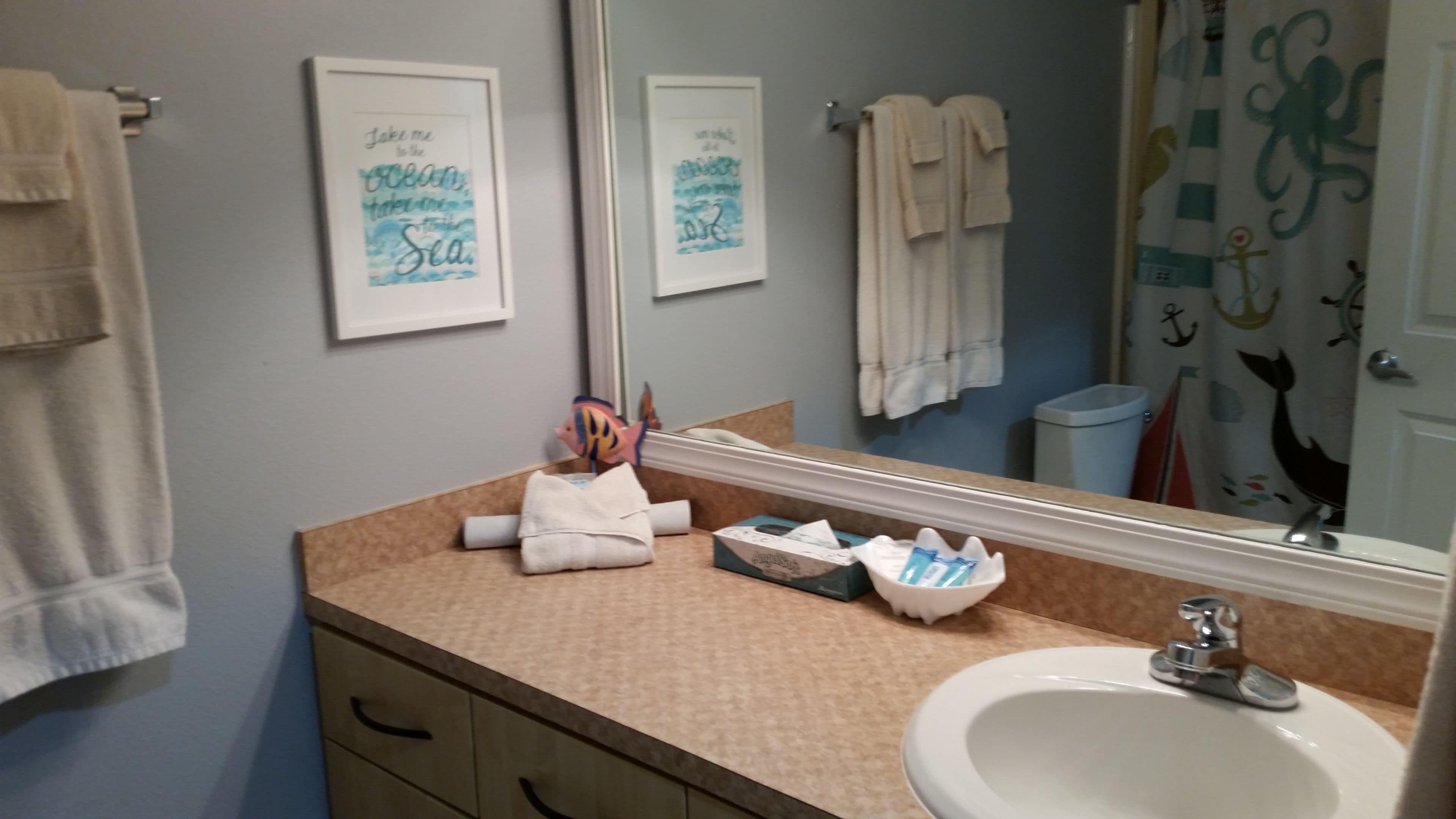 A bathroom with a sink, mirror, and towels. There are framed pictures on the wall and a shower curtain with sea animal designs.