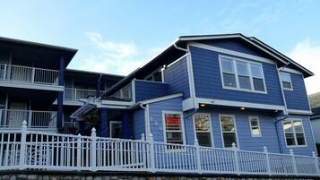 A two-story building with a blue exterior and white trim, featuring a balcony on the upper floor and a white picket fence in the foreground.