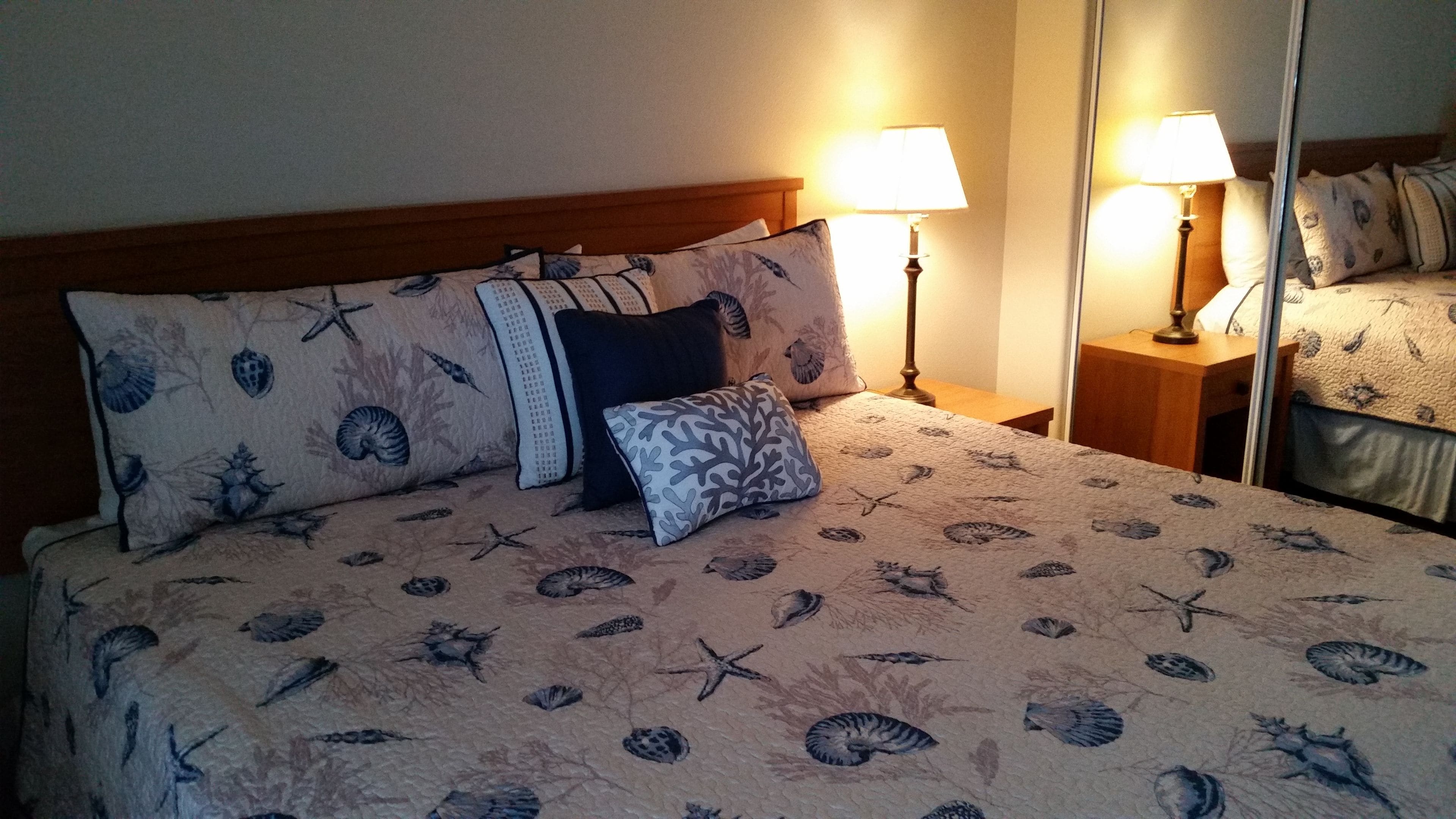 A bed with a floral and seashell pattern, flanked by two bedside lamps and a nightstand with a lamp.