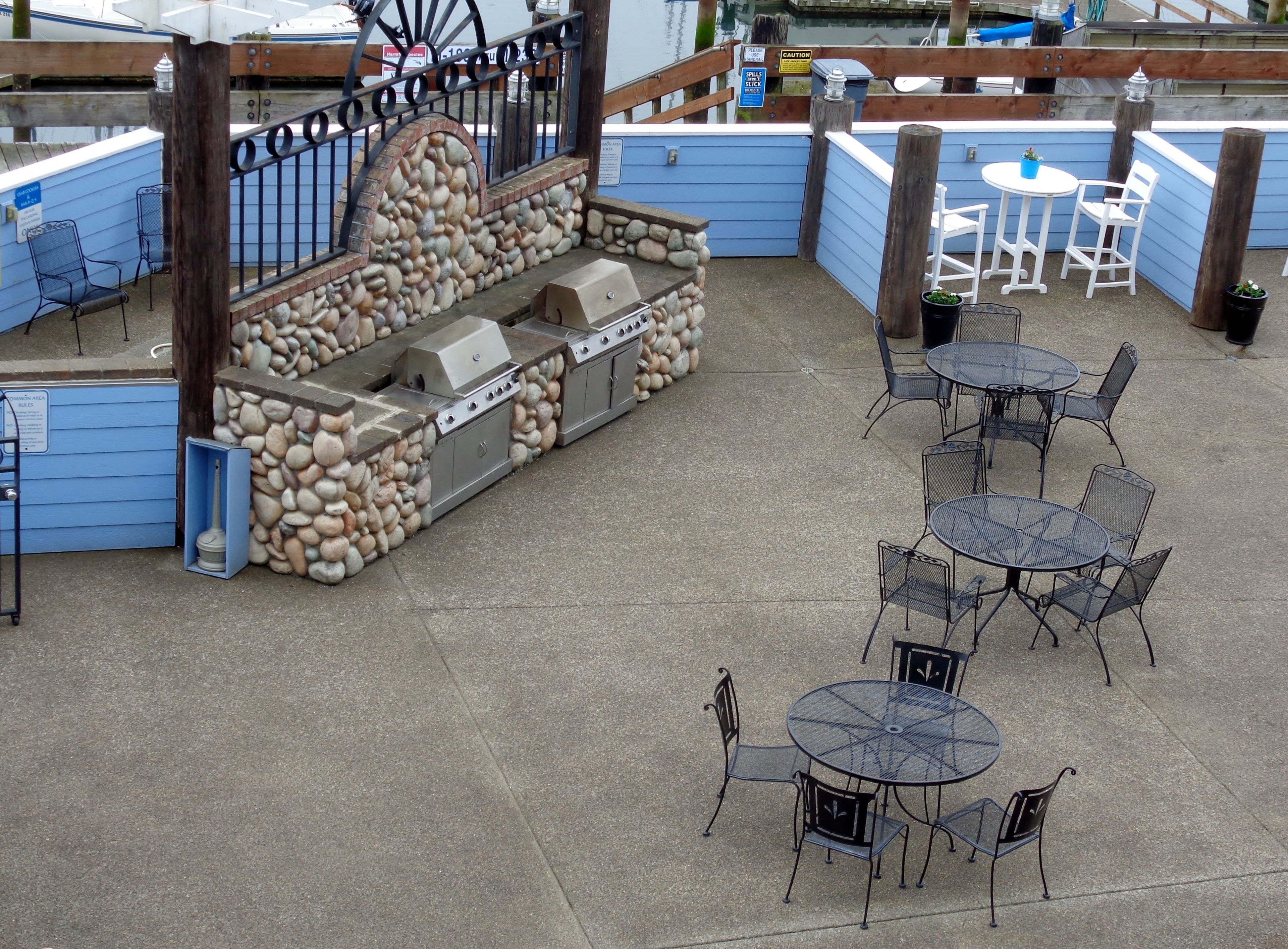 Un patio al aire libre con muros de piedra, una parrilla y mesas y sillas de metal.