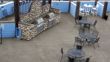 Un patio al aire libre con muros de piedra, una parrilla y mesas y sillas de metal.