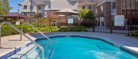 A swimming pool with a metal ladder, surrounded by a fence, and a building with a stone facade in the background.