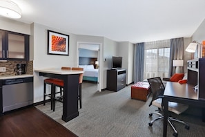A hotel room with a kitchenette, a bed, a desk, and a TV.