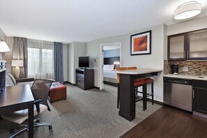 A hotel room with a desk, chair, kitchenette, and a bed. - Staybridge Suites Detroit-Utica by IHG (Utica)