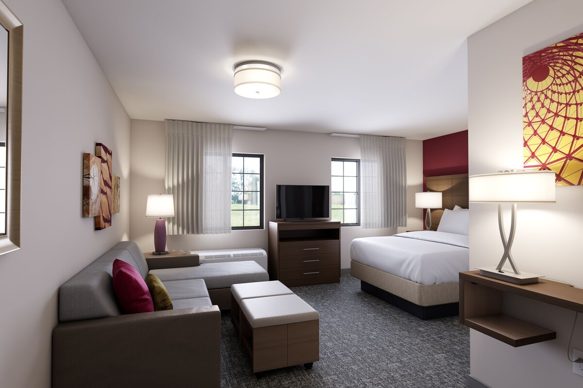 A hotel room with a sofa, a bed, a TV, a desk, and a lamp.
