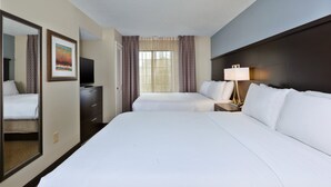 Una camera d'albergo con due letti, una TV, una scrivania con una lampada e uno specchio grande.