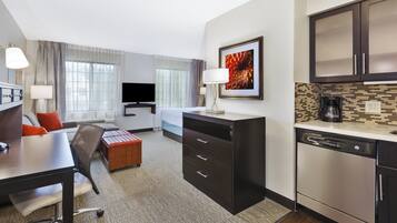 Una habitación de hotel con cama, escritorio, silla, kitchenette y televisor.