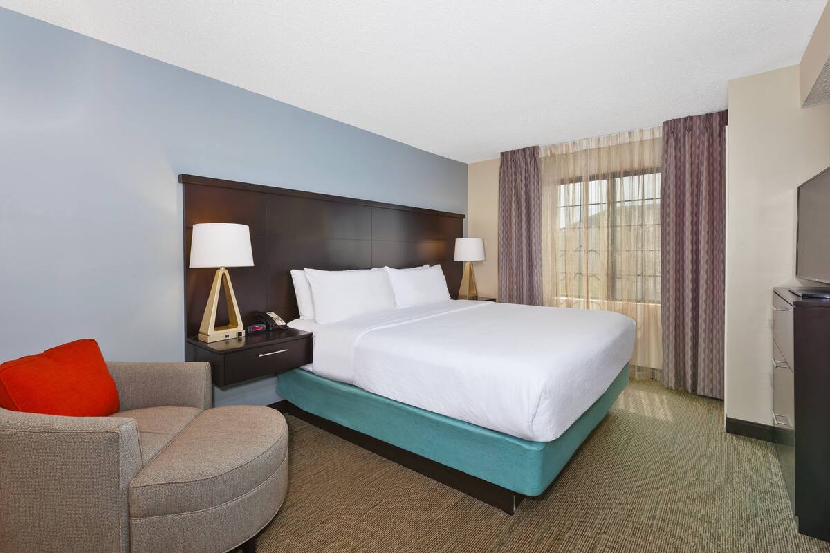 A hotel room with a bed, a nightstand, a lamp, a chair, and a television.