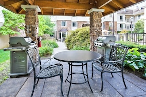 An outdoor patio with a round table and two chairs, a barbecue grill, and a fire extinguisher.