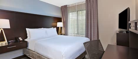 A hotel room with a large bed, bedside tables with lamps, a TV, and a desk.