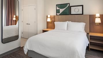 A hotel room with a large bed, a bedside table, a nightstand, a mirror, a door, and two wall-mounted lamps.