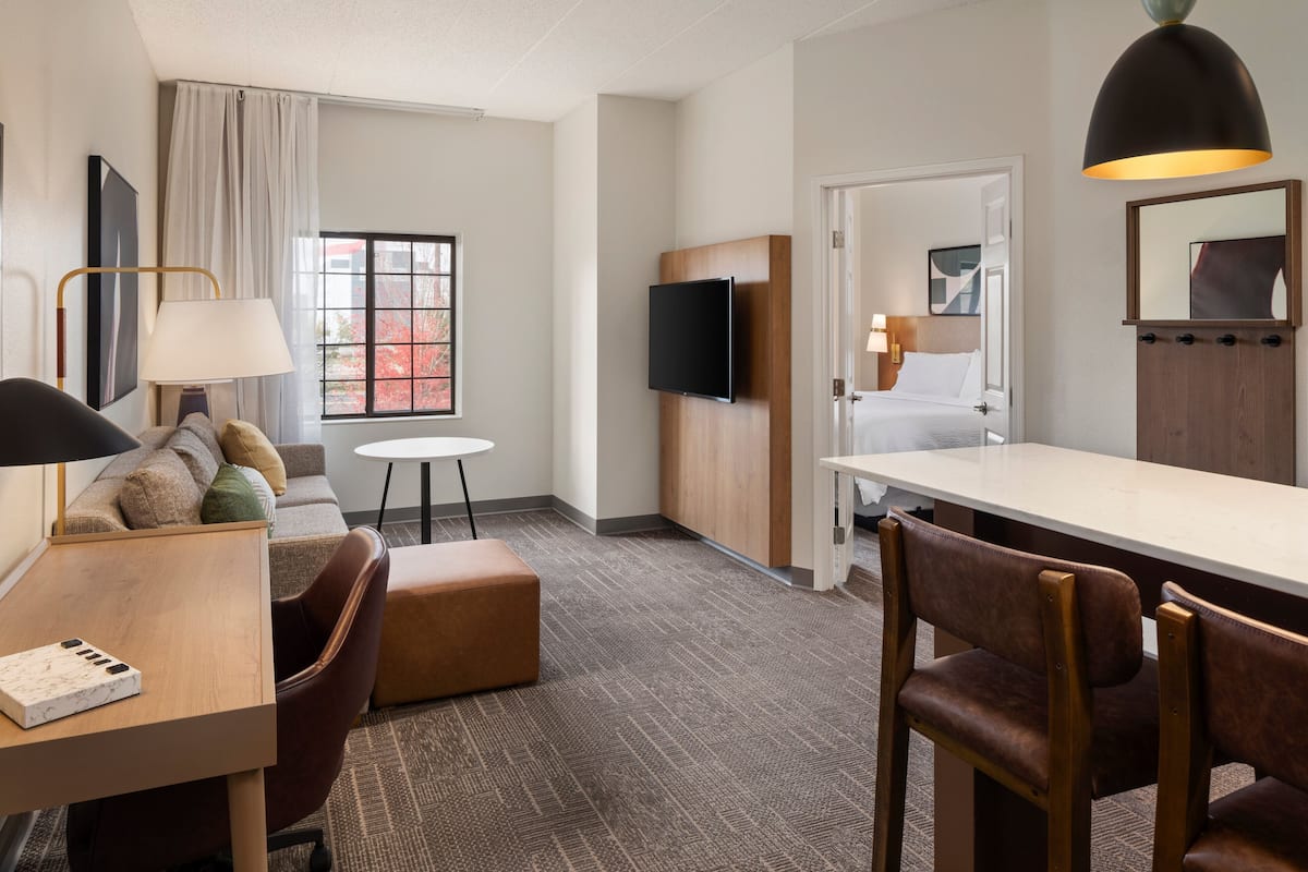 A hotel room with a bed, a TV, a desk with a lamp, a small table, and a sofa.