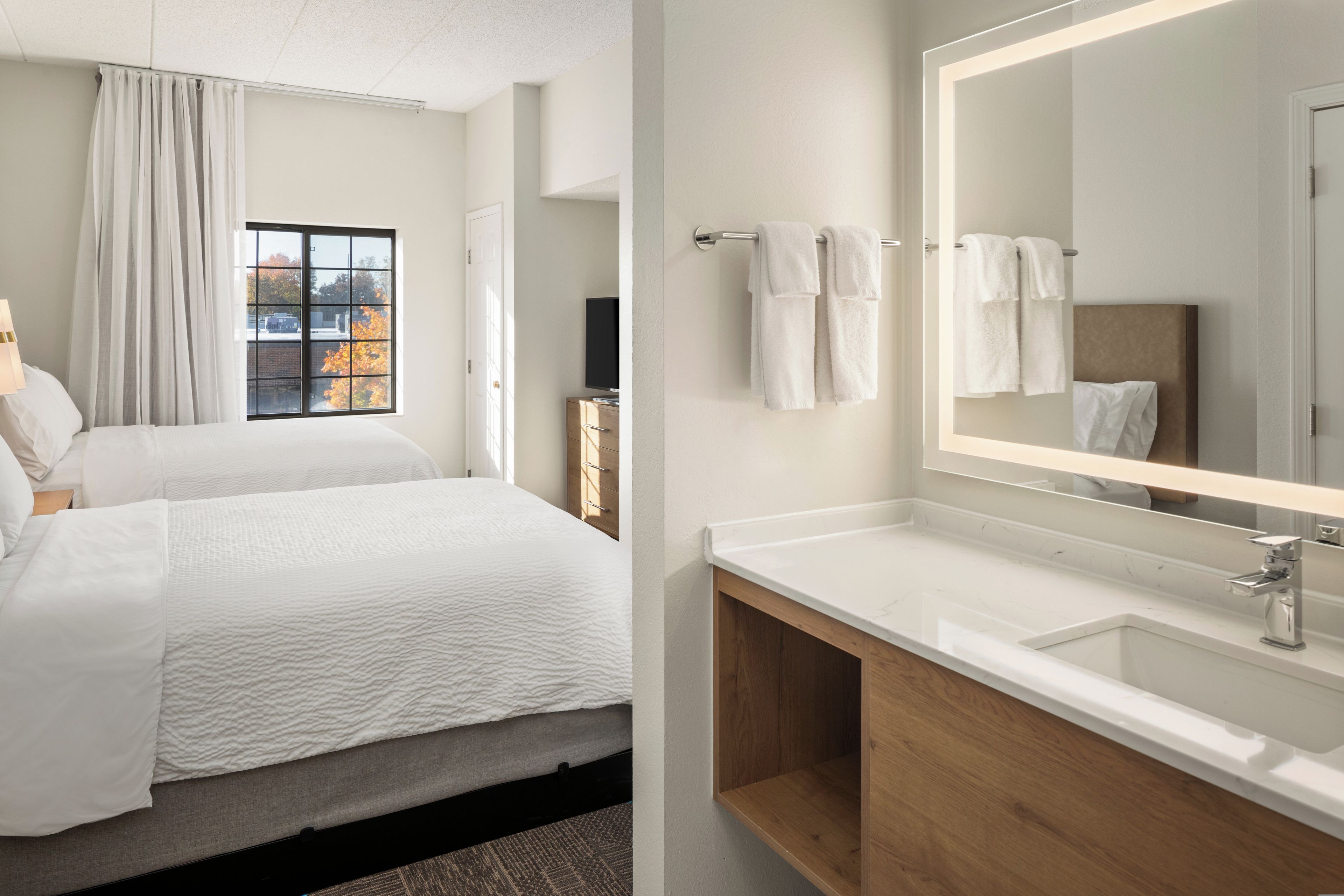 A hotel room with a bed, a bathroom with a mirror, and a window with curtains.
