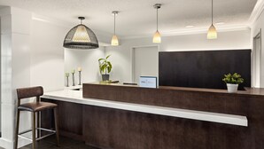 A reception area with a dark wood reception desk, a single chair, a potted plant, and a sign with the logo "IHG".