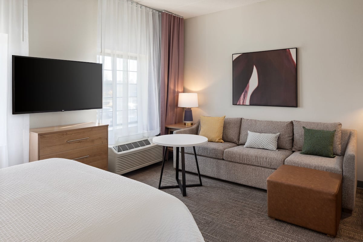 A hotel room with a large bed, a sofa, a small table, a TV, and a painting on the wall.