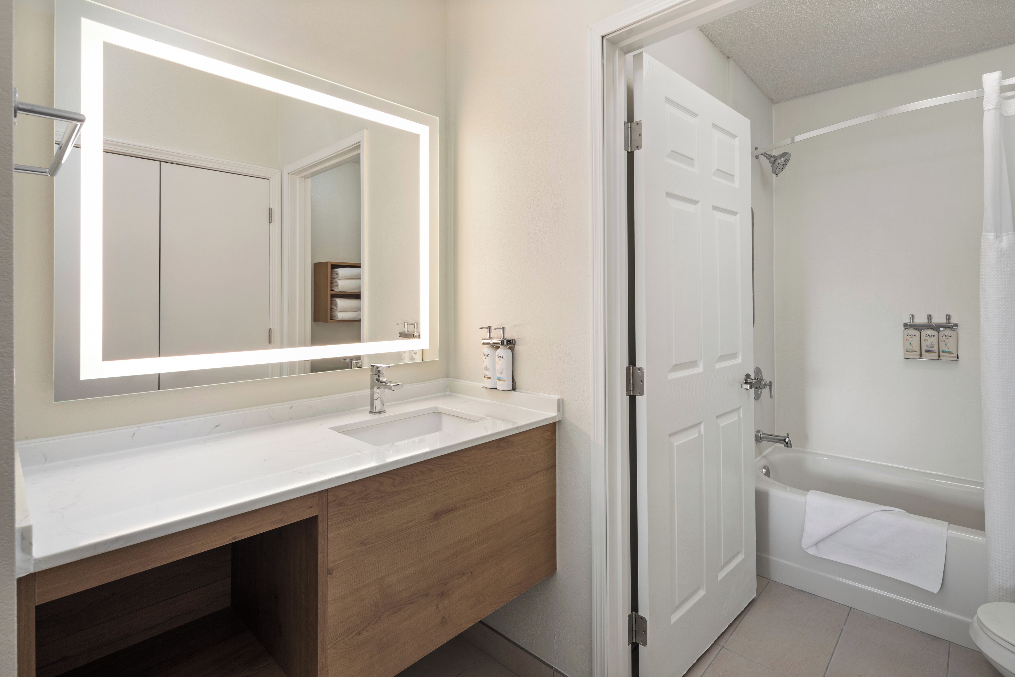 A modern bathroom with a large mirror, two sinks, a bathtub, and a shower.