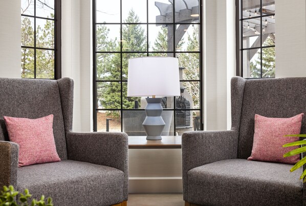 A corner seating area with two grey armchairs and a white lamp, positioned in front of a large window with a view of trees. - Staybridge Suites Minneapolis-Bloomington by IHG (Bloomington)