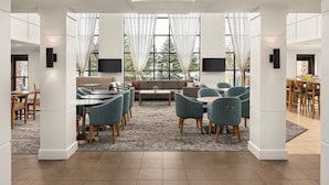 A spacious, well-lit room with a large dining area, comfortable seating, and large windows with sheer curtains.