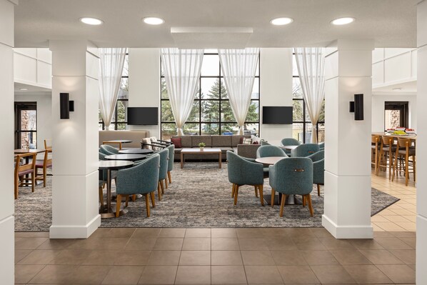 Una habitación amplia y luminosa con un comedor grande, asientos cómodos y ventanas amplias con cortinas translúcidas.