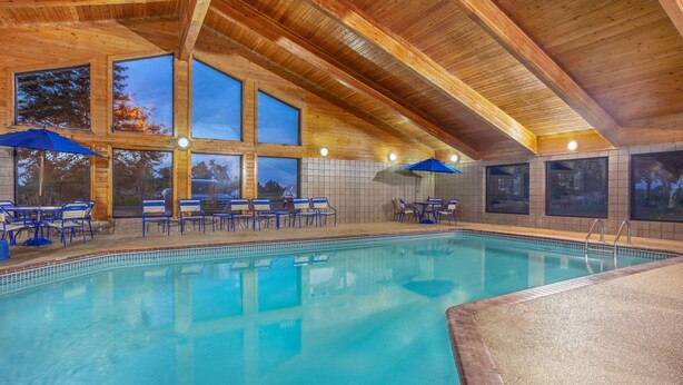 An indoor swimming pool with wooden beams, large windows, and blue umbrellas. - AmericInn by Wyndham Stillwater (Stillwater)