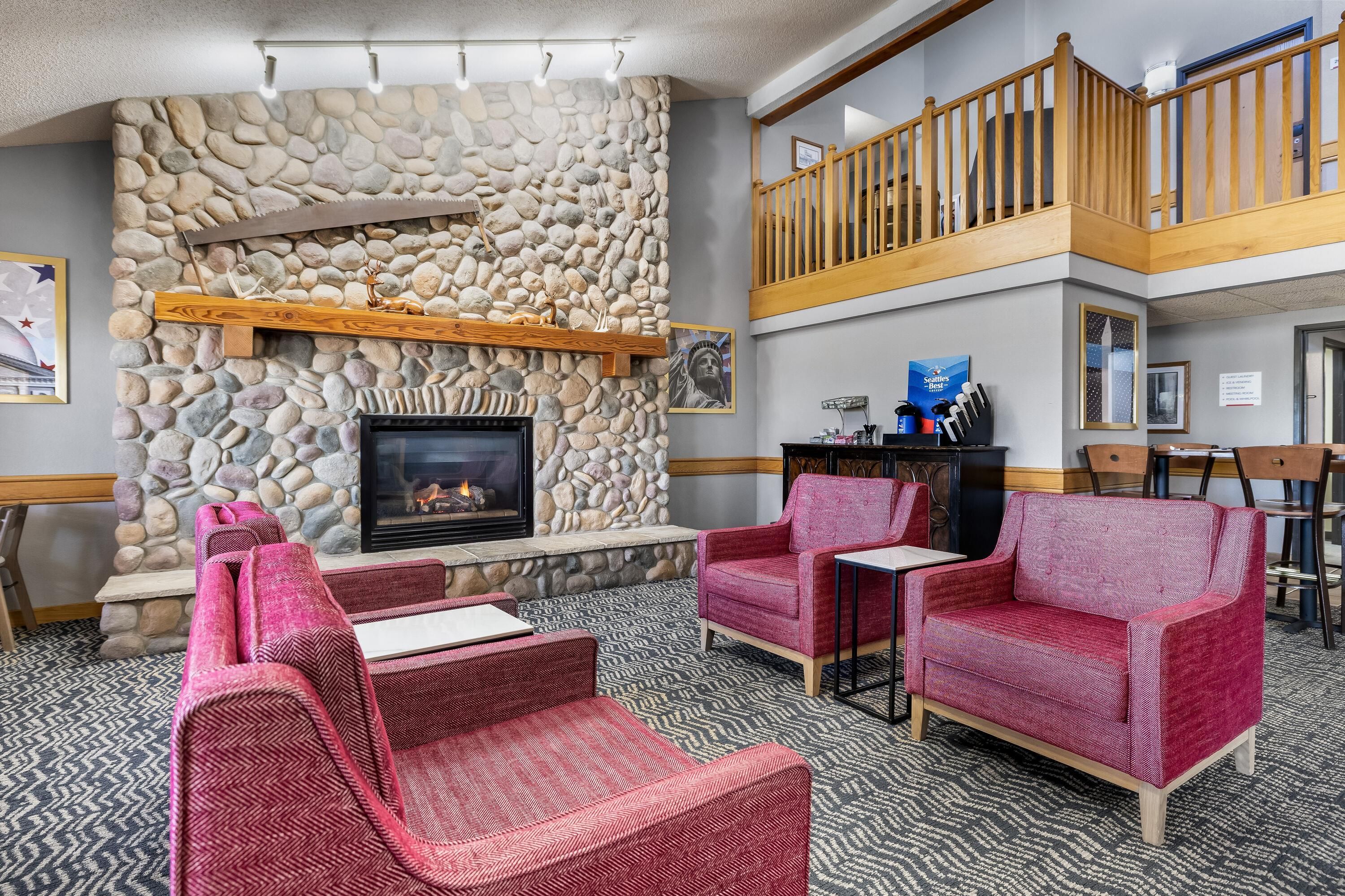Un hall d’hôtel doté d’une cheminée en pierre, de fauteuils à revêtement rouge, d’un escalier en bois et d’un comptoir de réception.