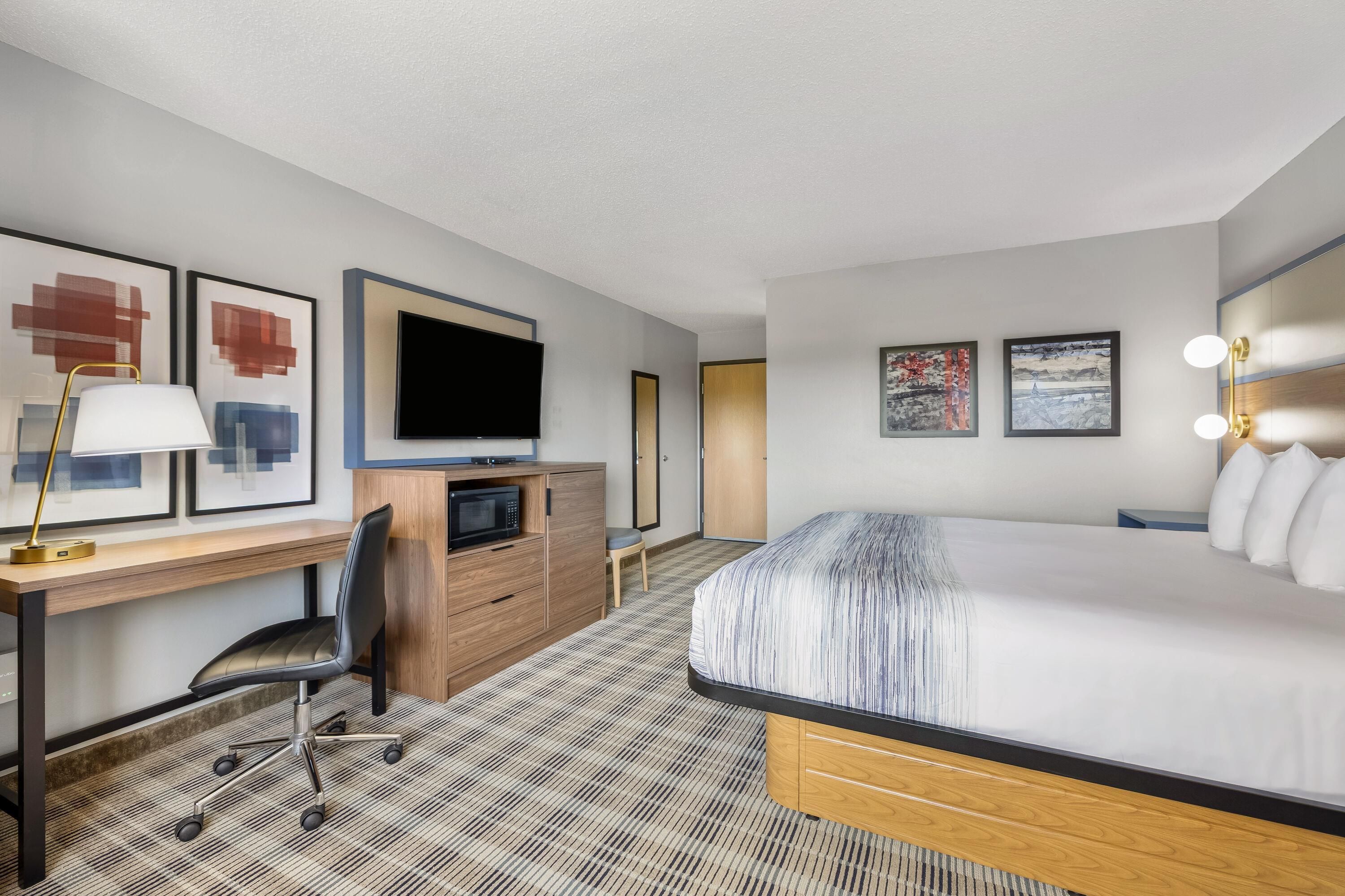 A hotel room with a bed, desk, chair, television, and artwork.