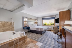 Quarto de hotel com cama grande, banheiro separado com banheira, área de estar com uma poltrona e janela com vista para o verde.