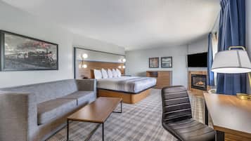 A hotel room with a bed, a sofa, a desk, a chair, a fireplace, and a television.