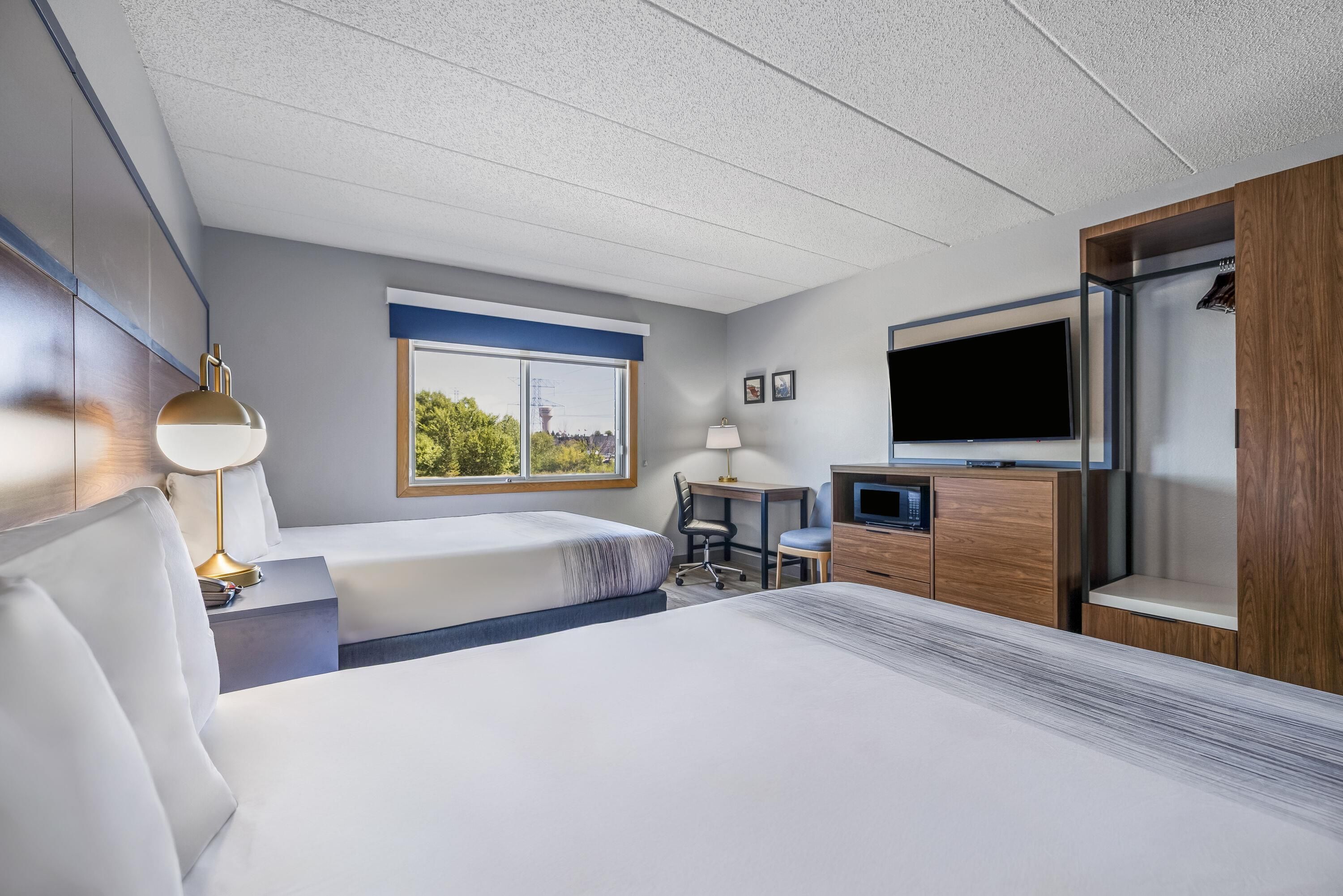 A hotel room with a bed, a desk, a TV, and a window with a view.